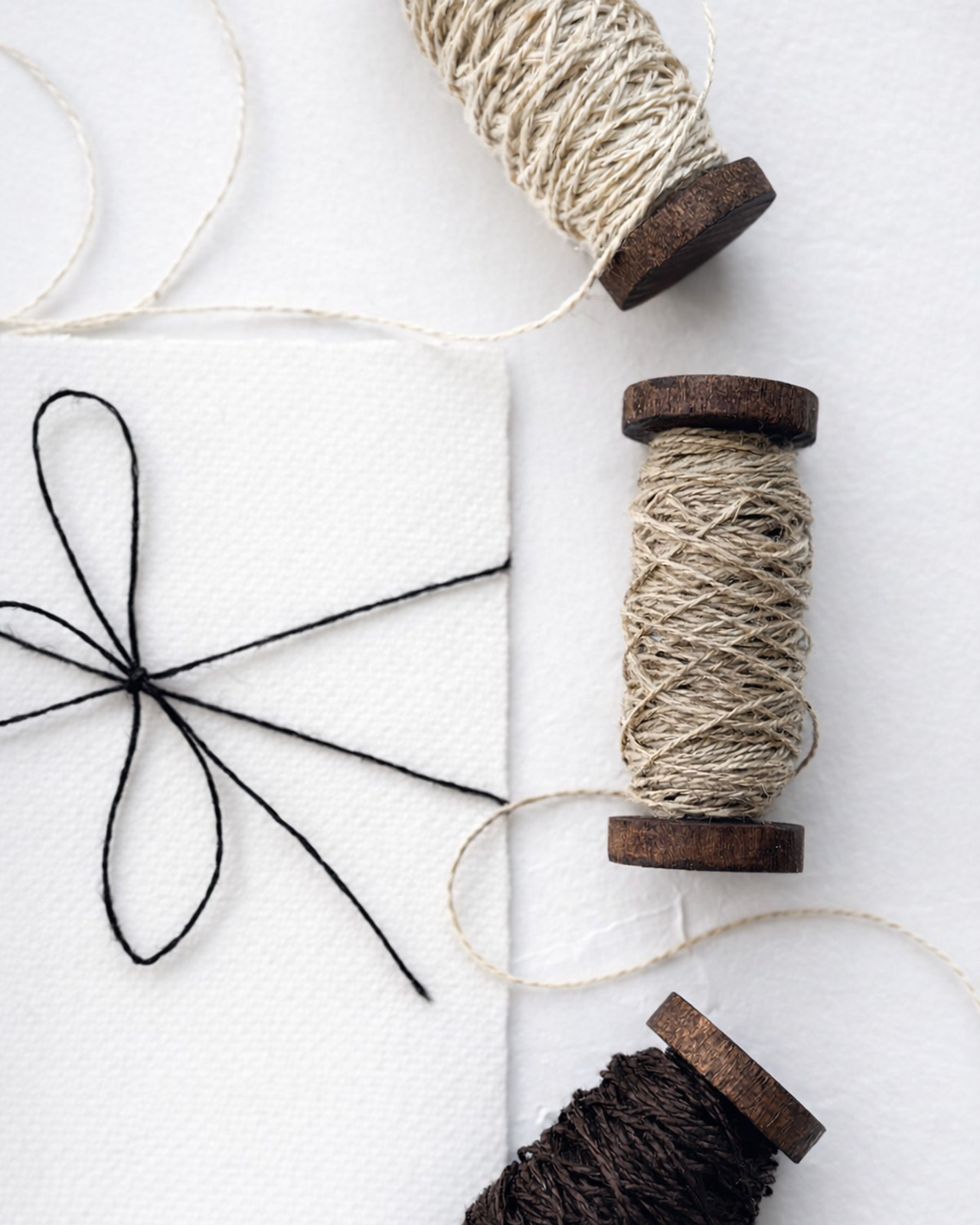Linen we-spun twine on vintage wooden spools for wedding invitations and stationery on white hand-made paper card